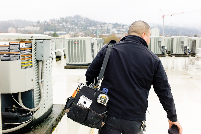 man carrying tool bag to fix roof top air conditioning units