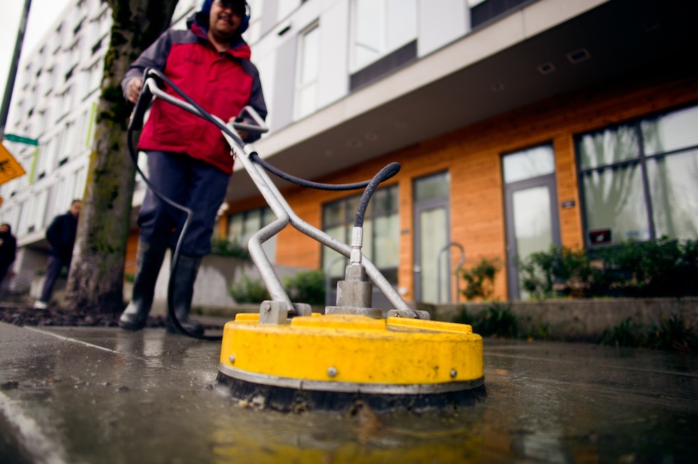 man cleaning sidewalk using sweeping machine